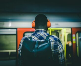 Pendler med oransje hodetelefoner og ryggsekk foran et tog