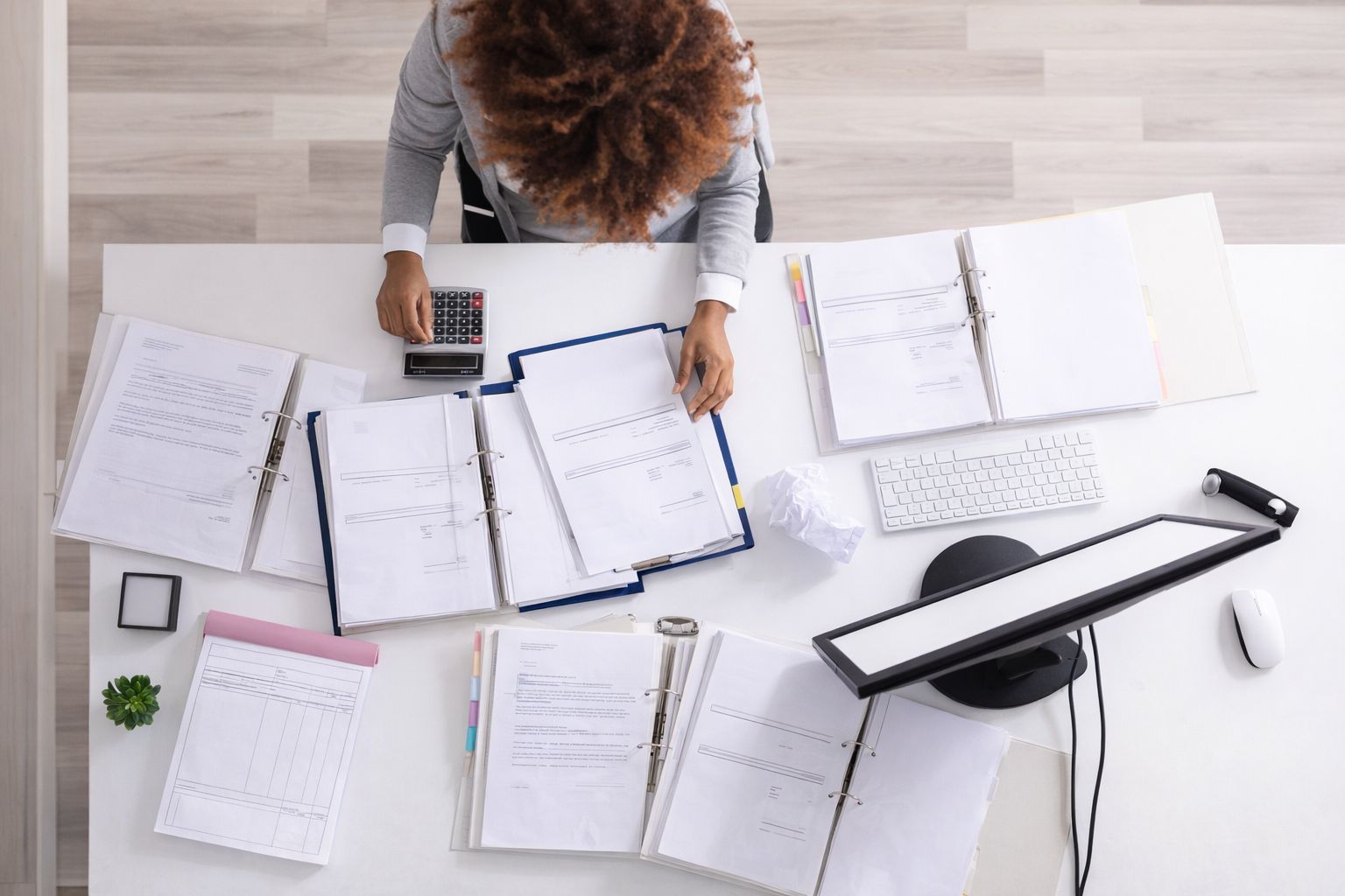 Kvinne går gjennom fakturaer og dokumenter ved et skrivebord sett ovenfra.
