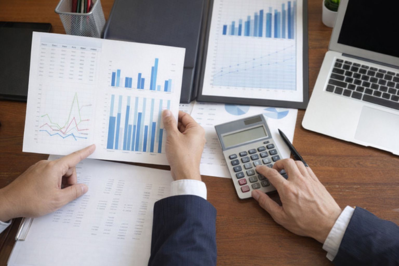 En person analyserer økonomiske grafer og bruker kalkulator på et kontor.